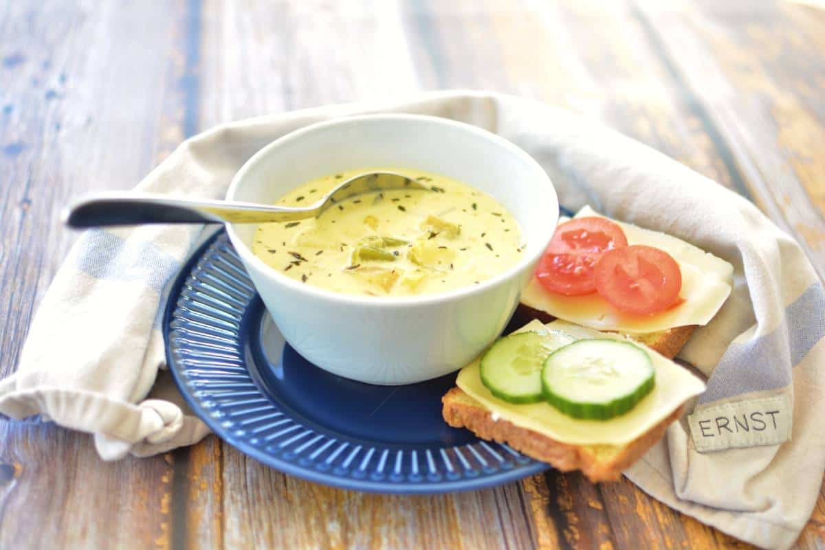 Spenatsoppa med ägg 9 En skål med soppa på en blå tallrik, med smörgåsar med ost, tomat och gurka bredvid.