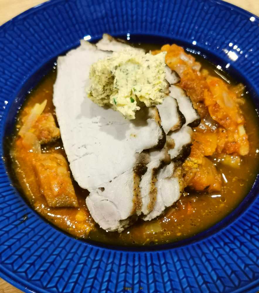 En skiva av kött serverad med sås och grönsaker på en blå tallrik.