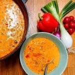 En skål med krämig tomatsoppa och en gryta med soppa samt grönsaker vid sidan.