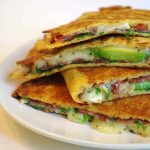 En tallrik med flera ost- och skinkquesadillas fyllda med avokado och grönsaker.