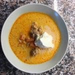 Skål med orange soppa innehållande köttfärs och gräddfil på toppen.