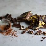 En portion chokladbrownies med marmorering och bitar av choklad på en yta med kakaopulver.
