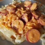Tallrik med pasta, skivad korv och en orange sås på toppen.